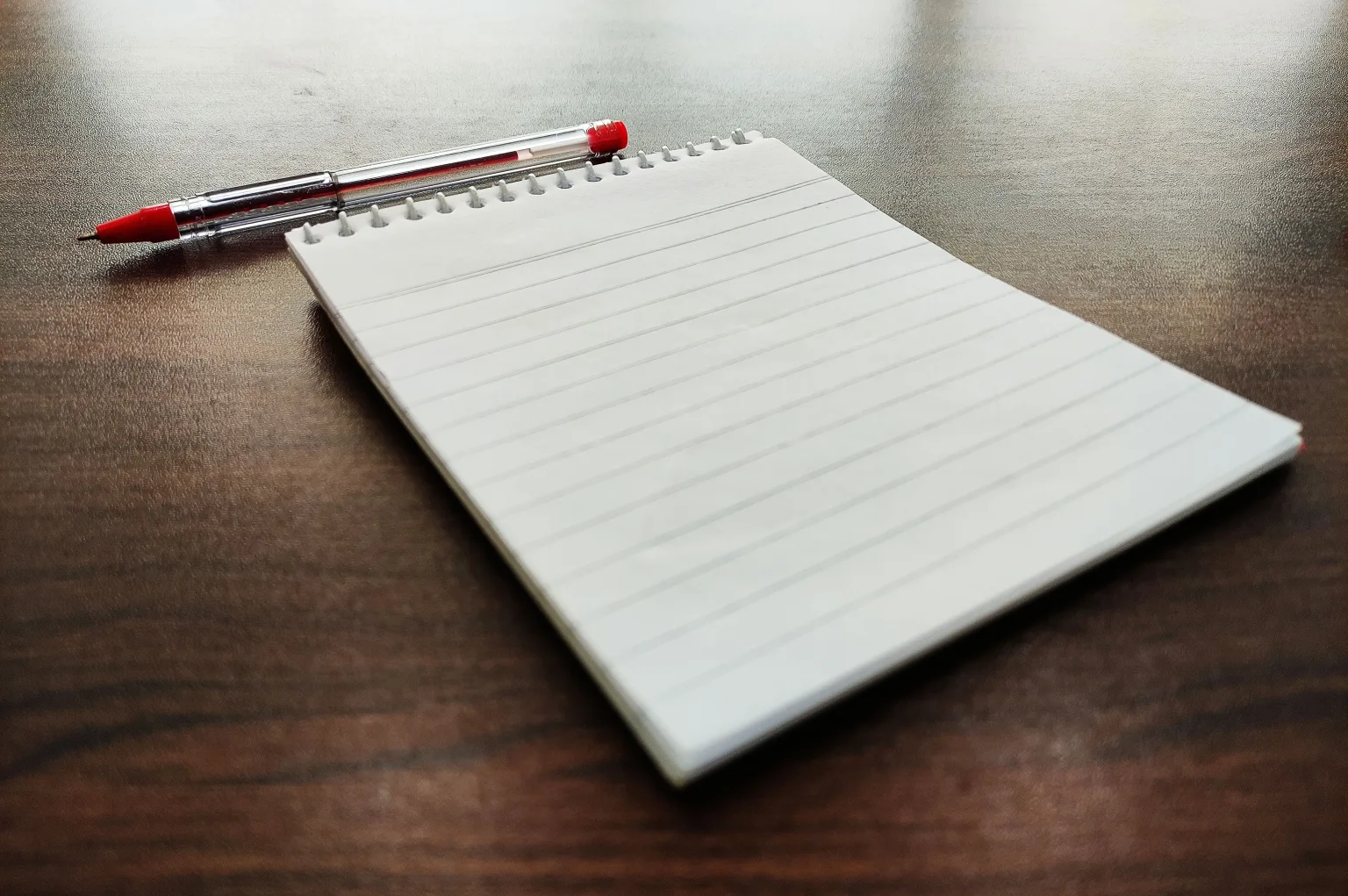 A blank spiral notebook and red pen on a wooden table.