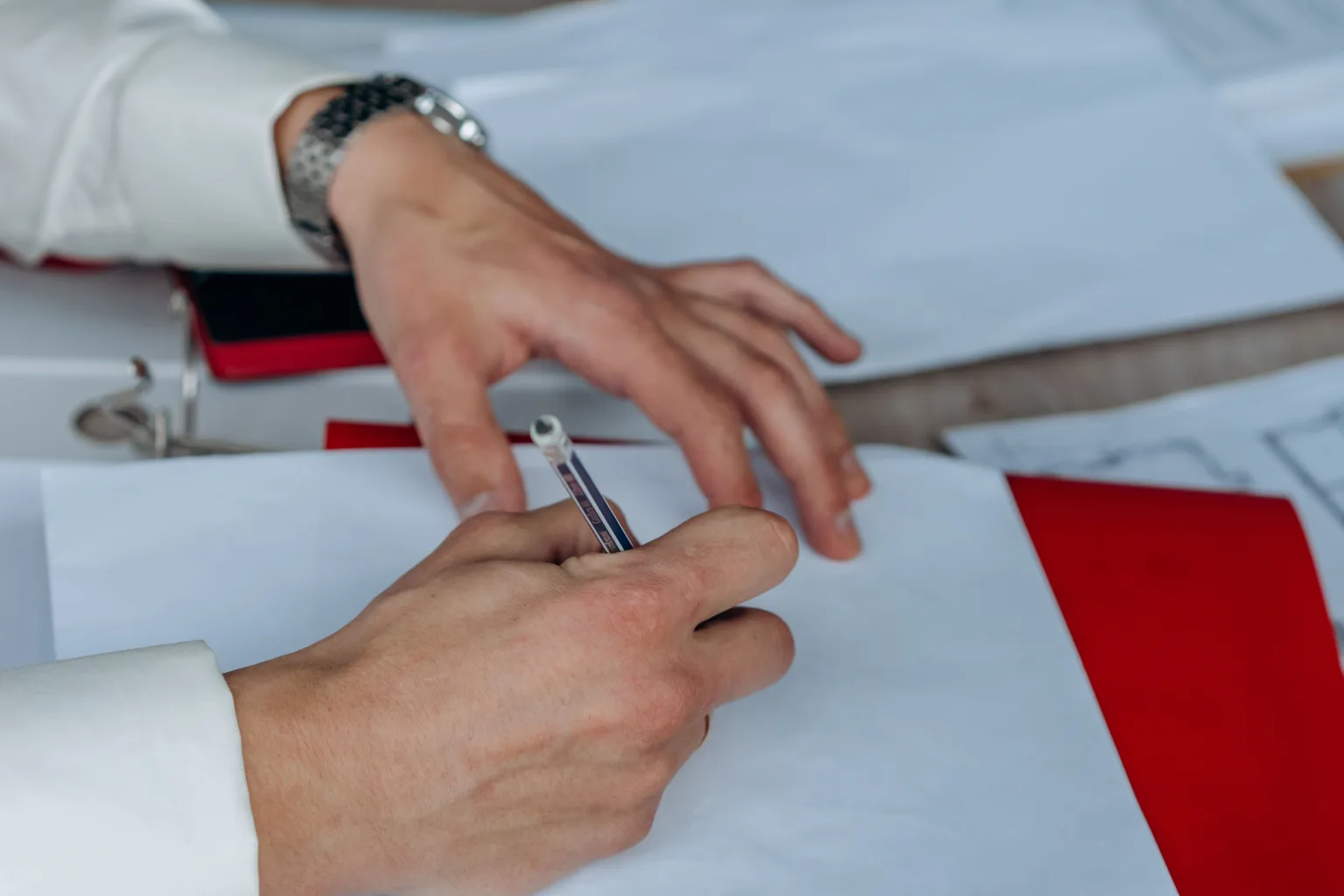 Hands writing notes on paper at a wooden table.